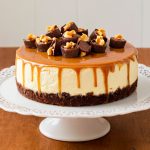 A decadent slice of Reese's Caramel Cheesecake topped with chocolate shavings and drizzled with caramel sauce.